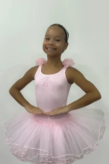 Pequena bailarina usando o Figurino Primeiros Passos Infantil rosa da Lucia Caliman, com saia de tule volumosa e detalhes florais no ombro, em uma pose clássica de ballet.