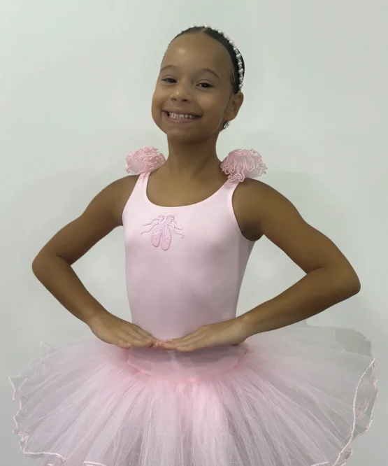 Pequena bailarina usando o Figurino Primeiros Passos Infantil rosa da Lucia Caliman, com saia de tule volumosa e detalhes florais no ombro, em uma pose clássica de ballet.