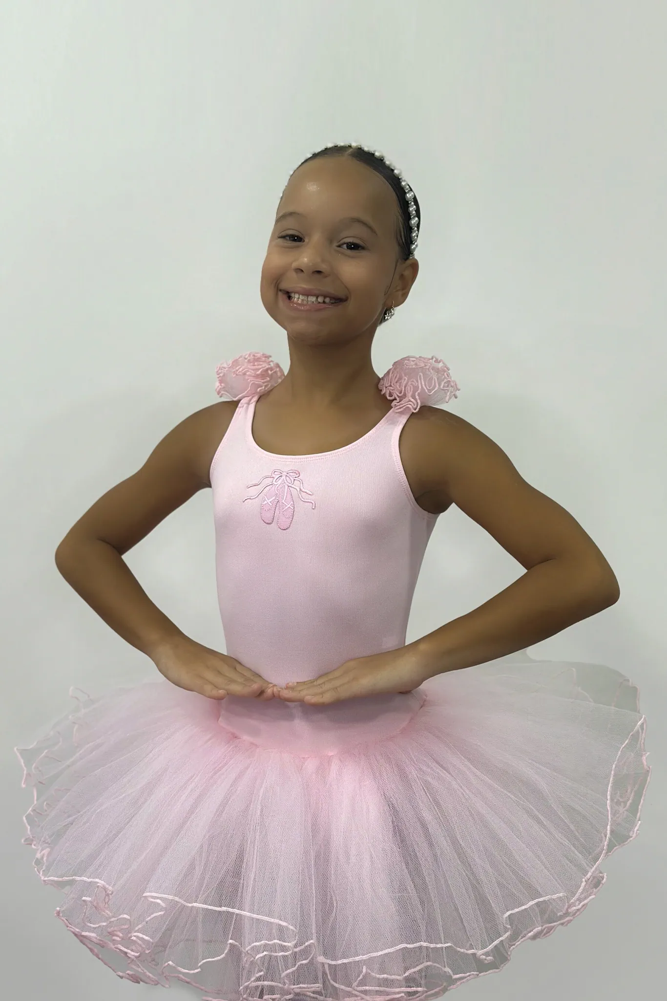 Pequena bailarina usando o Figurino Primeiros Passos Infantil rosa da Lucia Caliman, com saia de tule volumosa e detalhes florais no ombro, em uma pose clássica de ballet.