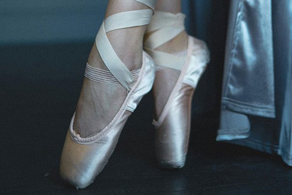 Close-up de pés femininos usando sapatilhas de balé, destacando a elegância e a técnica da dança clássica.