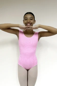 Jovem bailarina sorridente vestindo o Collant Aninha Infantil Candy rosa, de tecido canelado, em pose de dança com as mãos no quadril.