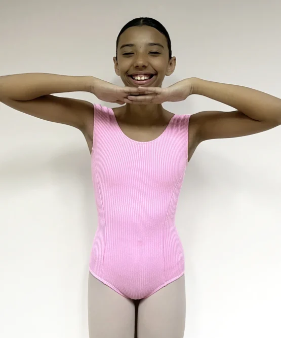 Jovem bailarina sorridente vestindo o Collant Aninha Infantil Candy rosa, de tecido canelado, em pose de dança com as mãos no quadril.