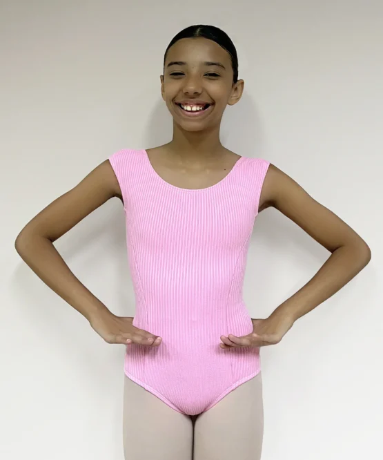 Jovem bailarina sorridente em pose de preparação vestindo o Collant Aninha Infantil Candy rosa, de tecido canelado, em pose de dança com as mãos no quadril.