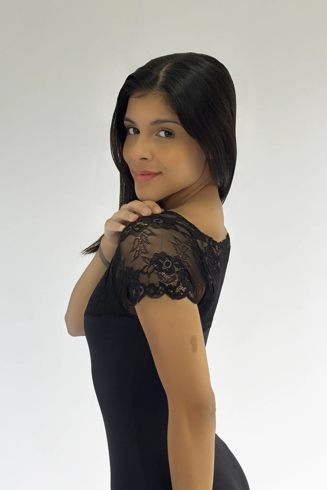 Vista lateral/costas de uma bailarina com o Collant 01.062 preto, destacando o design da manga de renda no ombro.