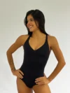 Bailarina de perfil vestindo o Collant 826 preto da Lucia Caliman, modelo com decote V e alças finas, em pose com as mãos na cintura.
