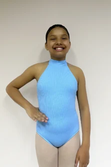 Vista frontal de uma jovem bailarina com a mão direita na cintura, vestindo o Collant Infantil Frente Única Azul Candy da Lucia Caliman