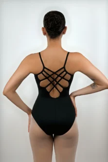 Bailarina de costas usando o Collant Alça Trançada preto da Lucia Caliman, exibindo o detalhe geométrico de múltiplas alças cruzadas nas costas abertas, em uma pose elegante com as mãos na cintura.