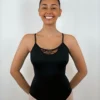 Bailarina sorridente usando o Collant Alça Trançada preto da Lucia Caliman, com as mãos nas costas, destacando o decote frontal que possui um delicado detalhe em renda floral.