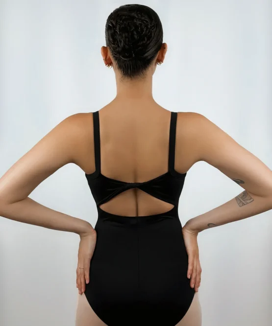 Bailarina de costas vestindo o Collant Costas Torcida preto da Lucia Caliman, exibindo o detalhe de tecido torcido no centro das costas nuas e as alças largas, em uma pose com as mãos na cintura.