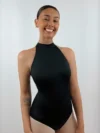 Bailarina de frente sorrindo e usando o Collant Frente Única Quatro Tiras preto da Lucia Caliman, destacando a gola alta elegante e o design sem mangas que valoriza os ombros.