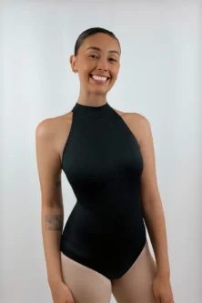 Bailarina de frente sorrindo e usando o Collant Frente Única Quatro Tiras preto da Lucia Caliman, destacando a gola alta elegante e o design sem mangas que valoriza os ombros.