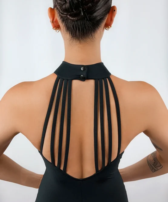 Bailarina de costas exibindo o Collant Frente Única Três Tiras preto da Lucia Caliman, com foco no design deslumbrante de tiras verticais nas costas nuas e na postura elegante com mãos na cintura.