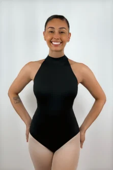 Bailarina sorrindo usando o Collant Frente Única Quatro Tiras preto da Lucia Caliman, destacando a gola alta elegante e o design sem mangas que valoriza os ombros.
