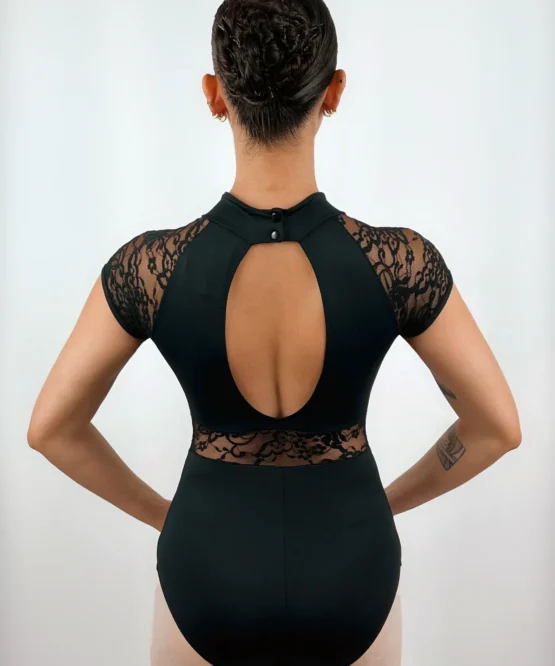 Bailarina de costas exibindo o Collant Manga Japonesa preto da Lucia Caliman. O foco está no elegante recorte oval nas costas nuas, nas mangas em renda floral, no fechamento por dois botões na nuca e no detalhe rendado que contorna a região lombar.