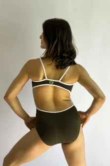 Vista posterior da modelo loira usando o Collant Marta verde com branco, destacando o recorte oval nas costas e a pequena bandeira do Brasil no centro.