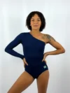 Modelo de pele retinta e cabelos cacheados vestindo o Collant Taty Azul da Lucia Caliman, peça de um ombro só com manga longa em malha canelada e detalhe da bandeira do Brasil.