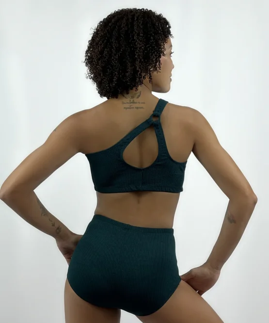 Dançarina em pose firme de costas vestindo o Top Daiane verde escuro da Lucia Caliman, destacando o design elegante de um ombro só.