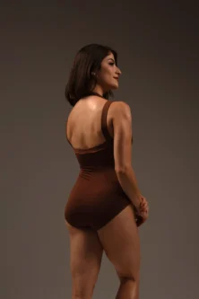 Modelo de perfil de costas usando Collant Duna marrom, exibindo o recorte reto nas costas e o ajuste firme no corpo.