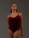 Bailarina de frente vestindo o Collant Marta vinho da Lucia Caliman. A imagem destaca o caimento perfeito da malha canelada e o recorte vazado nas costas com faixa de sustentação.