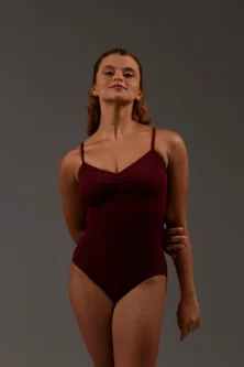 Bailarina de frente vestindo o Collant Marta vinho da Lucia Caliman. A imagem destaca o caimento perfeito da malha canelada e o recorte vazado nas costas com faixa de sustentação.