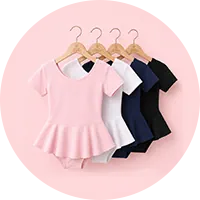 Cinco leotards infantis com saia rodada pendurados em cabides de madeira, nas cores rosa, branco, azul marinho e preto, sobre fundo rosa claro.