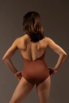 Bailarina de costas usando o Collant Frente Única caramelo da Lucia Caliman, com as mãos repousando na cintura para mostrar o caimento anatômico.